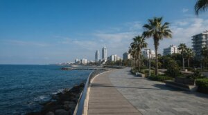 טיילת חוף מרוצפת לצד מי ים כחולים ומבני מגורים מודרניים באור יום מלא בלימסול